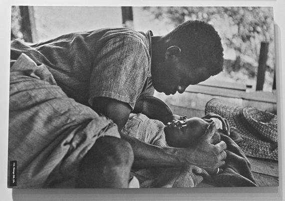 Black and white photograph of a man leaning down to his baby lying in front of him, holding its head with his hands.
