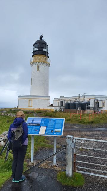 Cape Wrath lighthouse. The foreground shows an information board, with somebody reading it.