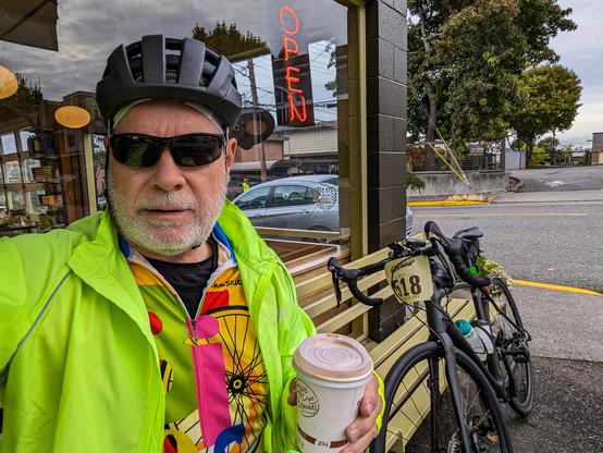 Man in colorful cycling attire drinking coffee outside Walnut Street Coffee in Edmonds WA. His bicycle is in the background.