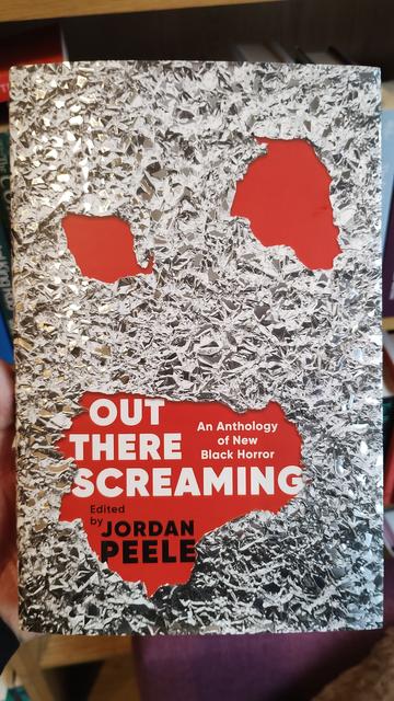 Cover to Out There Screaming, editied by Jordan Peele, artwork like a rippled, bashd piece of cooking aluminium foil, ripped to infer eyes and a mouth.