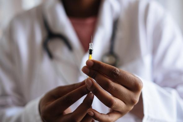 Close up shot of a needle in the hands of a medical professional wearing a white lab coat.