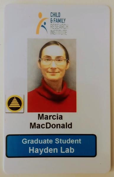 ID Card for Marcia MacDonald, graduate student in the Hayden lab at the Child & Family Research Institute (with logo). Photo shows a person with pale skin, dark hair pulled back, glasses, a slight smile, and a red sweater.
