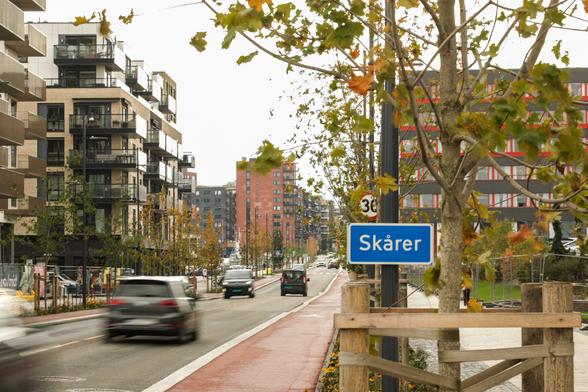Foto som viser Skårer etter skiltet å dømme, med boligblokker ca 6 etasjer høye, muligens næring i første, og opphøyd sykkelfelt i veien, fartsgrense 30: Trær plantet langs veien (dessverre mellom sykkelfelt og fortau heller enn mellom sykkelfelt og kjørefelt).