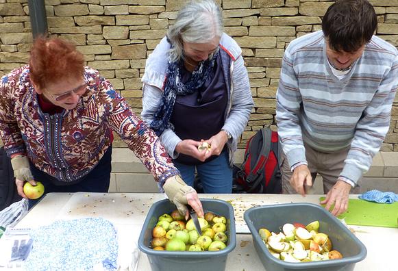 Three people behind a table are washing and cutting apples in preparation for juicing.