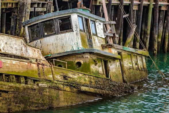 This is an image of an old fishing boat. This boat was moored at Noyo Harbor in Ft. Bragg California.
The boat sank in a storm back a few years ago. It has since deteriorated even more.
The hull is sticking out of the water at an odd angle as the boat is sitting on the bottom of the river near a boat ramp. One of the planks that makes up the hull is missing. There is a green mold thatis taking over the boat as it grows up towards the cab from the river. Most of the paint has pealed off the wooden structure and there are a couple of broken windows.
Behind the boat is the dock that it was once tied up to.