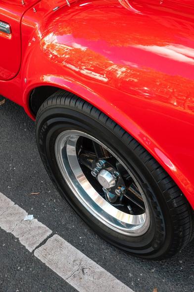 photo of the left back tire of a Shelby Cobra 427 oldtimer with red chassis, on dry asphalt
