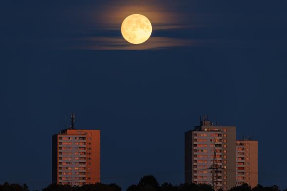 Der Vollmond geht hinter Schleierwolken über drei Hochhäusern auf.