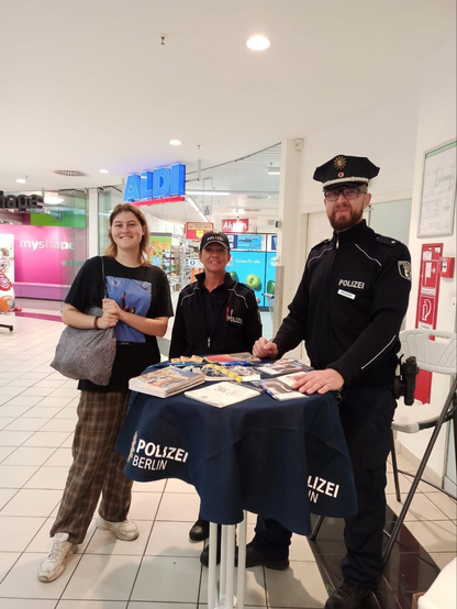 Polizist, Polizistin und eine Frau stehen an einem Präventionsstand.