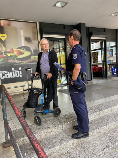 Polizist und Bürger vor einem Supermarkt.