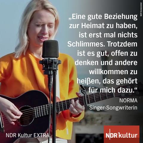 Foto der Sängerin NORMA am Mikrofon mit einer Gitarre in der Hand.

Dazu das Zitat: "eine gute Beziehung zur Heimat zu haben, ist erst mal nichts Schlimmes. Trotzdem ist es gut, offen zu denken und andere willkommen zu heißen, das gehört für mich dazu." NORMA, Singer-Songwriterin