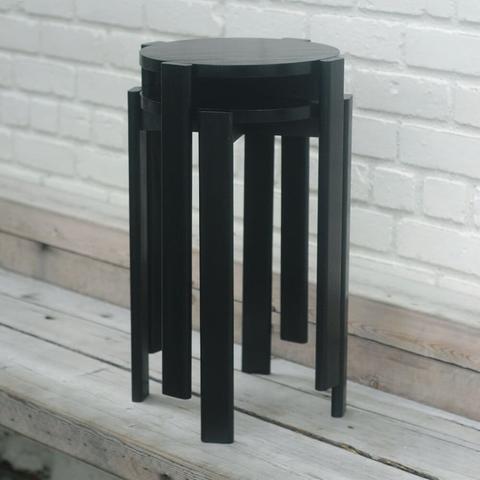 Two poplar stools stacked on top of each other. The legs nest in order to pack tightly together. They are stained black.
