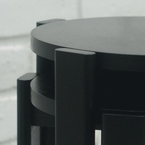 A close up of the seats of two poplar stools stacked on top of each other. The legs nest in order to pack tightly together. They are stained black.