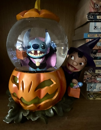 A Lilo and Stitch themed snowglobe, with Lilo dressed as a witch and Stitch dressed for Halloween as a very cute vampire. Sits on the shelf with my beloved Discworld books.