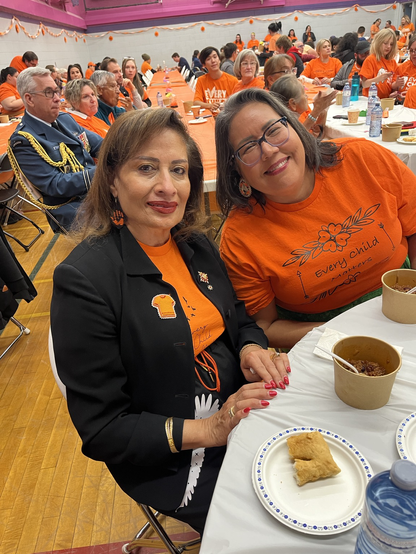 Alberta Lieutenant Governor Salma Lakhani, in an orange shirt and navy blazer, sits next to Cheryl Whiskeyjack, the CEO of Bent Arrow who also wears a bright orange shirt that reads Every Child Matters.