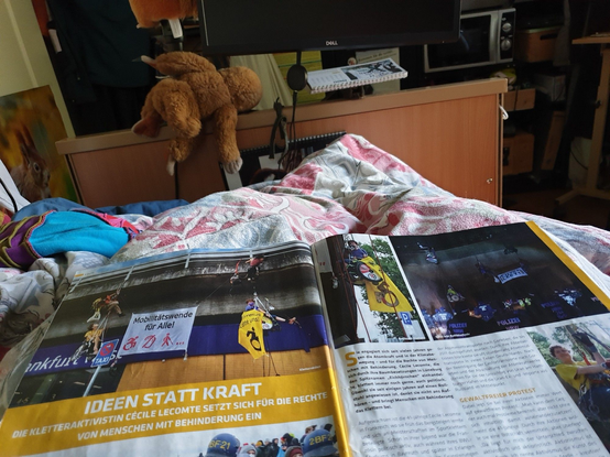 Magazin auf ein bett geöffnet, 2 Seiten des Artikels auschnittweise zu sehen, überschrift "Ideen statt Kraft, die Kletteraktivistin Cécile Lecomte setzt sich für die Rechte von Menschen mit Behinderung ein. und Bild einer Aktion am bhf Ffm West 2 Menschen im Rollstuhl und 2 ohne klettern an der Fassade in Seilen und haben ein Banner "Mobilitätswend für alle", recht ein Bild von mir im Seil mit Rollstuhl und Megafon, ein bild einer Abseilaktion in Lützerath mit Banner Lützi lebt, bei Nacht, ein Auschnitt eines Bildes aus dem besetzen Walt Altibleibt