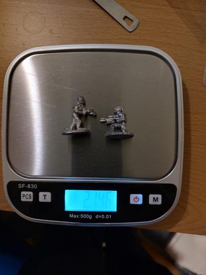 Two corroded gaming miniatures in a scale, which reports they have 21.46 grams of mass.