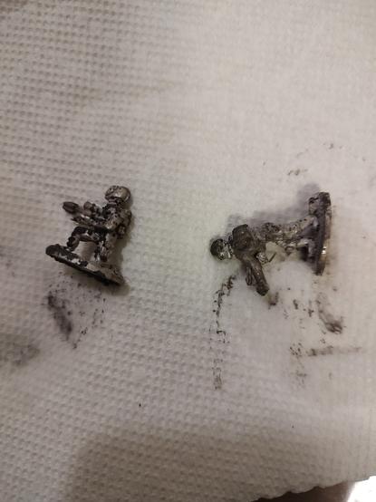 Two corroded gaming miniatures in a paper towel. Parts of the total are stained black by corrosion coming off the miniatures.