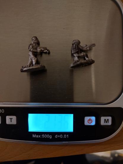 Two corroded gaming miniatures in a scale, which reports they have 21.36 grams of mass.