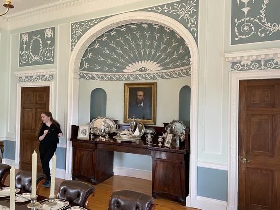 Portrait of CSP above the original sideboard in a dining room alcove. Fine original plasterwork with blue background (CSP hated the earlier green). Guide Sarah points out the details.