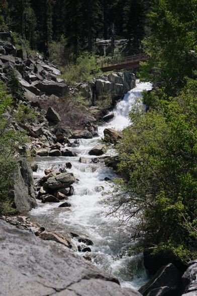 A fast stream with a waterfall under a bridge.