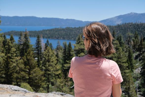 A young woman looking at a lake, photographed from behind.