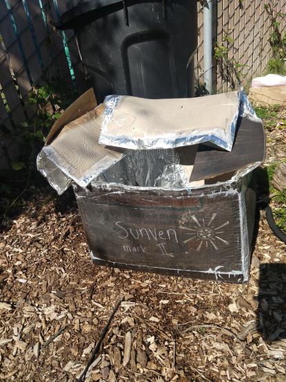 Picture of my cardboard solar oven looking very sad, the reflectors have folded over and the cardboard is slumped and wavy from being soaked in water.