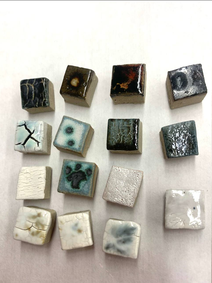 Eight square glazed ceramic tesserae, each with a unique finish. Some have crackling in the shape of lightening. The surfaces can be matte, glossy, metallic, or bubbly. Colors range from light to dark, some with speckles in yellow and dark teal resembling the appearance of mold or cheese.