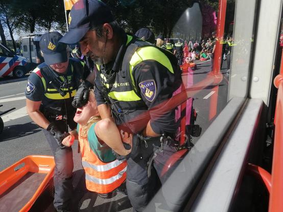 Twee agenten pakken een geweldloze demonstrant hardhandig aan door polsen om te buigen en de neus achterover te trekken.