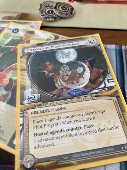 AstroScript Pilot Program; a long-rotated Netrunner card, with a homemade clear acrylic moon token atop it.