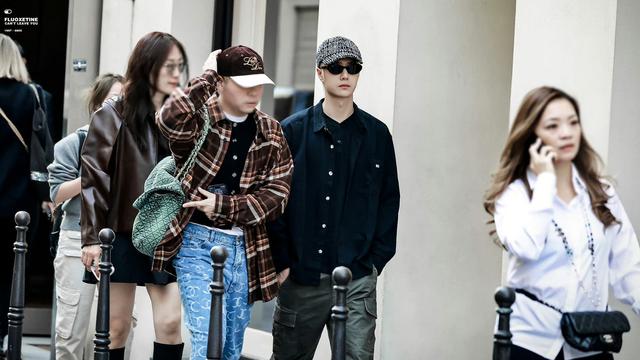 Wang Yibo at Chanel flagship store in Paris. he has platinum blond hair under a tweedy baseball cap. he's wearing black sunglasses and a rumpled, oversized black shirt.