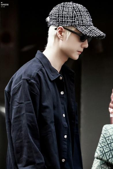 Wang Yibo at Chanel flagship store in Paris. he has platinum blond hair under a tweedy baseball cap. he's wearing black sunglasses and a rumpled, oversized black shirt.