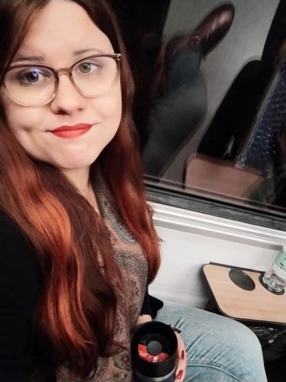 A selfie one the train with a thermos in hand. I don't look happy.