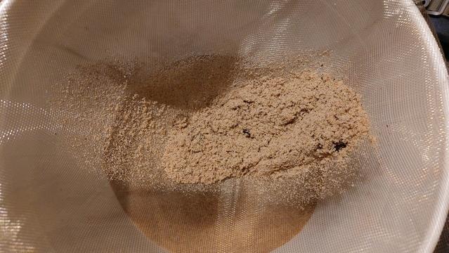 A small pile of sand sits a top a bit of screening which itself is a top a white bucket.
