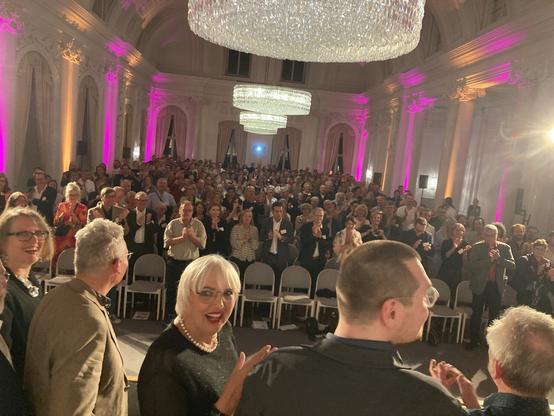Standing Ovation für die besten Buchhandlungen Deutschlands. Im Vordergrund steht Kulturstaatsministerin Claudia Roth, links von ihr zwei Vertreter der Jury Britta Jürgs und Christian Geschke (https://www.deutscher-buchhandlungspreis.de/jury/)