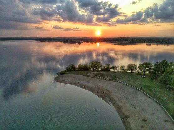 Sun sets with clouds colored orange and yellow over a lake, taken with a drone