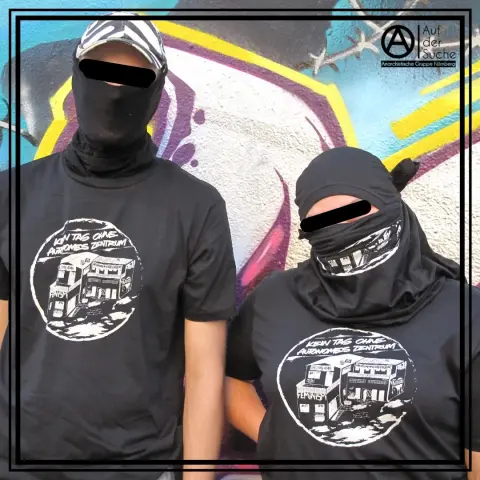 Zwei vermummte Menschen tragen die P31 Soli Shirts. Das Motiv zeigt das Autonome Zentrum und dem Schriftzug Kein Tag ohne Autonomes Zentrum