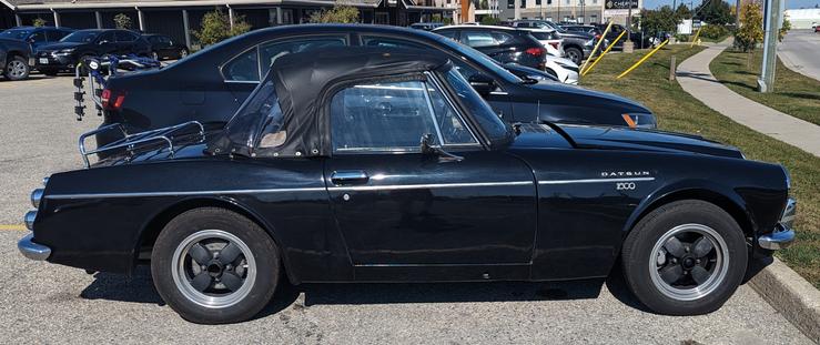 A classic Datsun 1600 ragtop in black sideview. A nice roadster from over 50 years ago.