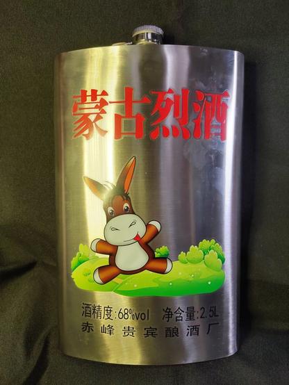 Front of the flask removed from its case with a cartoon donkey sitting on grass.  (The brand name is translated literally to "stuffy donkey" but more idiomatically, perhaps, as "drunken ass".)