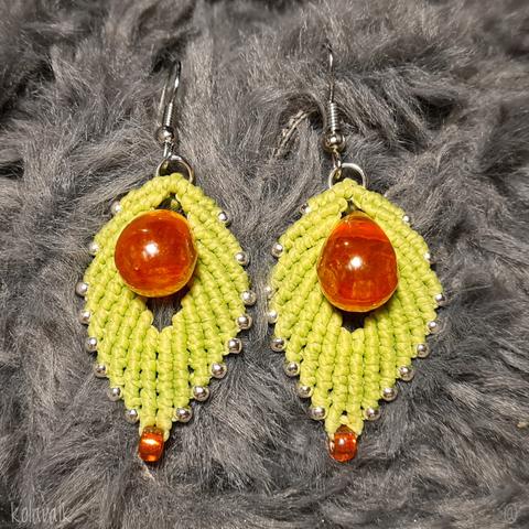 Détail des deux boucles d'oreilles côte à côte, posées sur une matière grise duveteuse. On voit bien la forme de feuilles vertes avec la perle de verre orange au centre.
