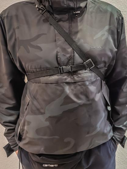 Person wearing a three point camera strap over a camouflage jacket. Seen from the front.