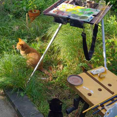 Cats harassing artist while painting in a garden.