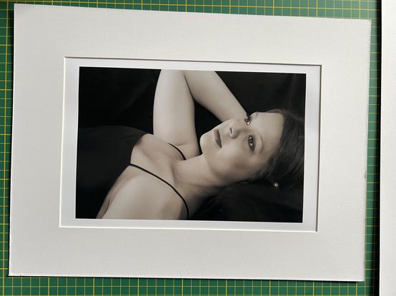 Mounted sepia-toned photograph, of a woman reclining, looking up, away from the camera. Her right arm is raised, with her hand behind her head.