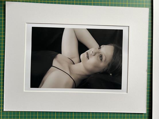 Mounted sepia-toned photograph, of a woman reclining, looking up, away from the camera. Her right arm is raised, with her hand behind her head.