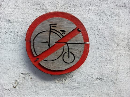 Ein historisches Holzschild signalisiert in Zons "Fahrradfahren verboten" mit einem Hochrad. Vermutlich ein Entwurf eines humorvollen Stadtmitarbeiters.