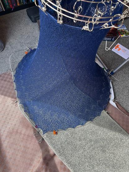 A navy lace knitted skirt being blocked with pegs and wires