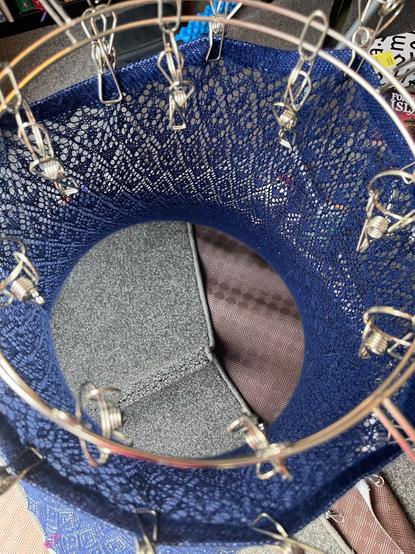 Top down view of a knitted lace skirt being blocked. Shows the pegs it is hanging from.