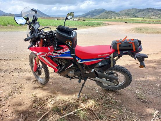 My damaged Honda CRF300 Rally. The left fairings are cracked and torn in multiple locations, having snapped their plastic lugs or snapped right off the bolts. The toolbox, also located on the left of the bike, is being held together with a strap.