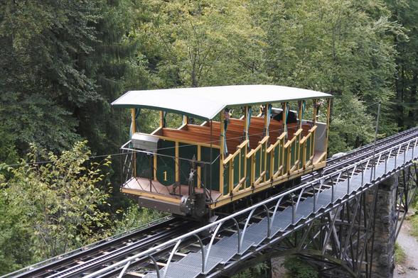 Photo of the Giessbachbahn funcular, showing a carriage riding over a steel bridge in the midst of woodland.