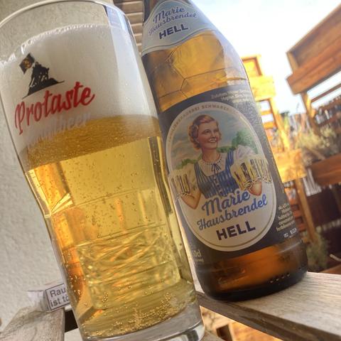 Sonntags auf Balkonien. Ein Glas Helles, dahinter die Flasche, auf der Marie freudig Bierkrüge zu uns durstigen Männern bringt. Im Hintergrund ein spärlich besetztes Pflanzenregal worauf die Nachmittagssonne scheint.