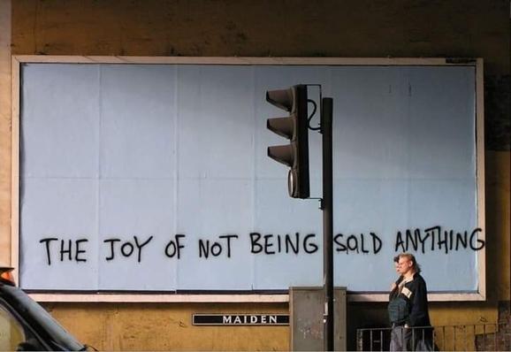 A blank billboard with graffiti saying "the joy of not being sold anything"